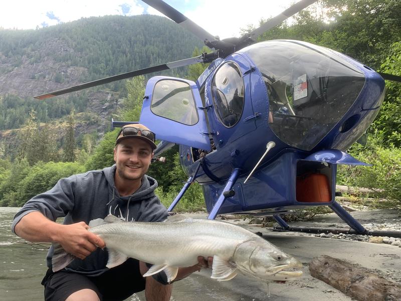 Angler holding a large fish in front of a blue helicopter.