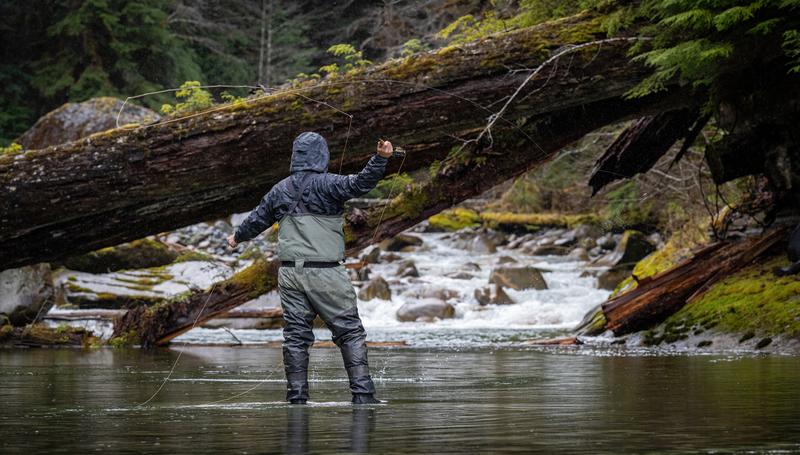 Man standing in a river holding a large fish he caught with a helicopter in the background