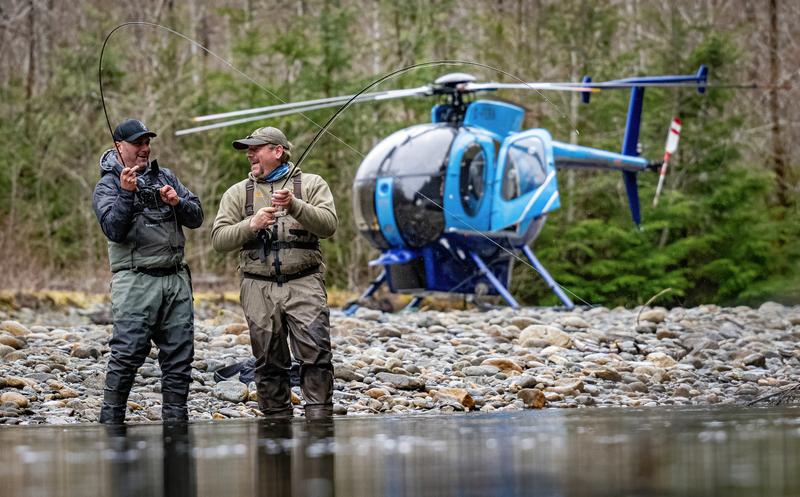 Two men fishing in a river with a helicopter in the background