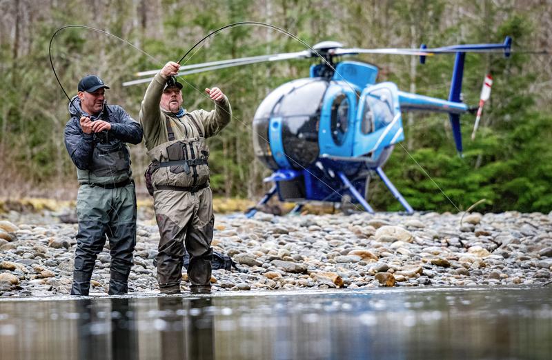 Two anglers standing in a river celebrating a catch with a blue helicopter behind them.