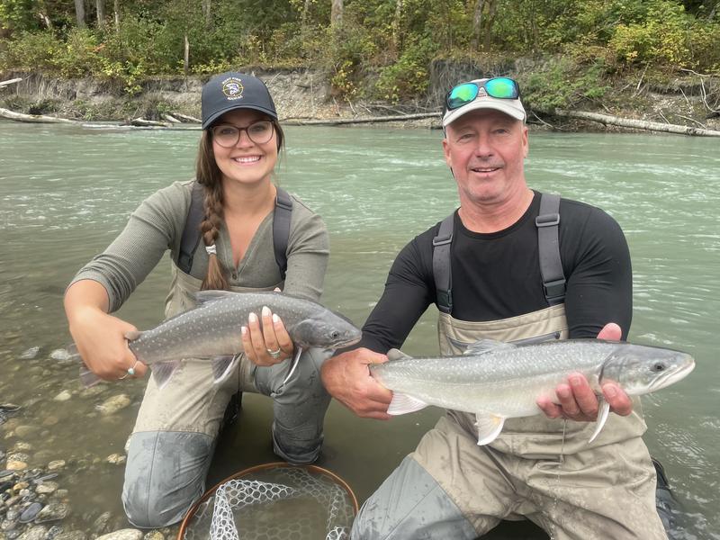Two anglers in waders holding a salmon in a river.
