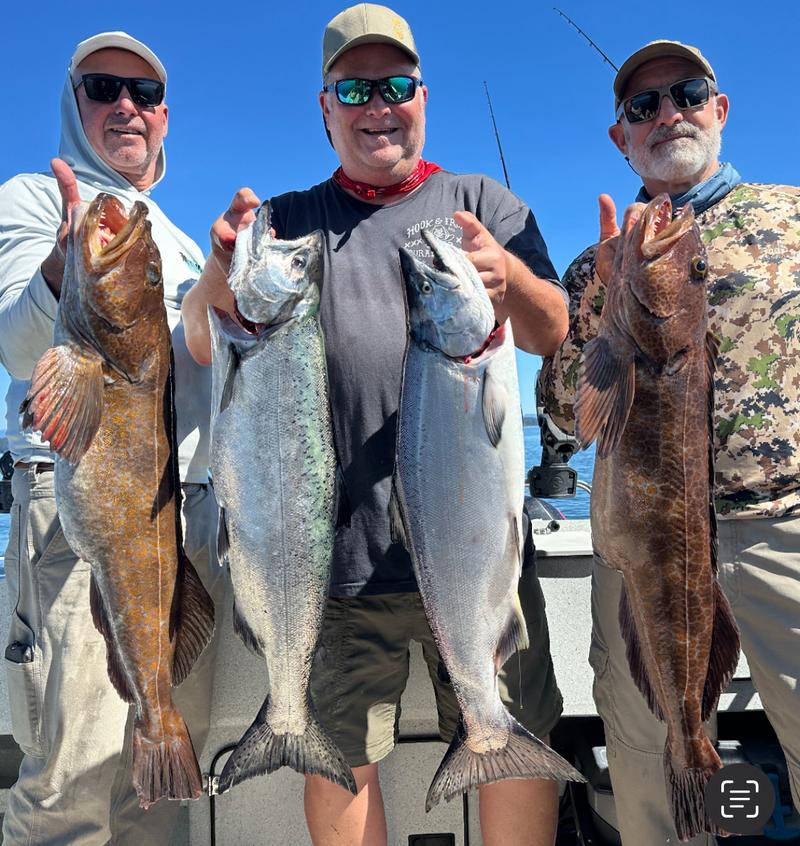 Three anglers on a boat holding up their catch of salmon and lingcod.