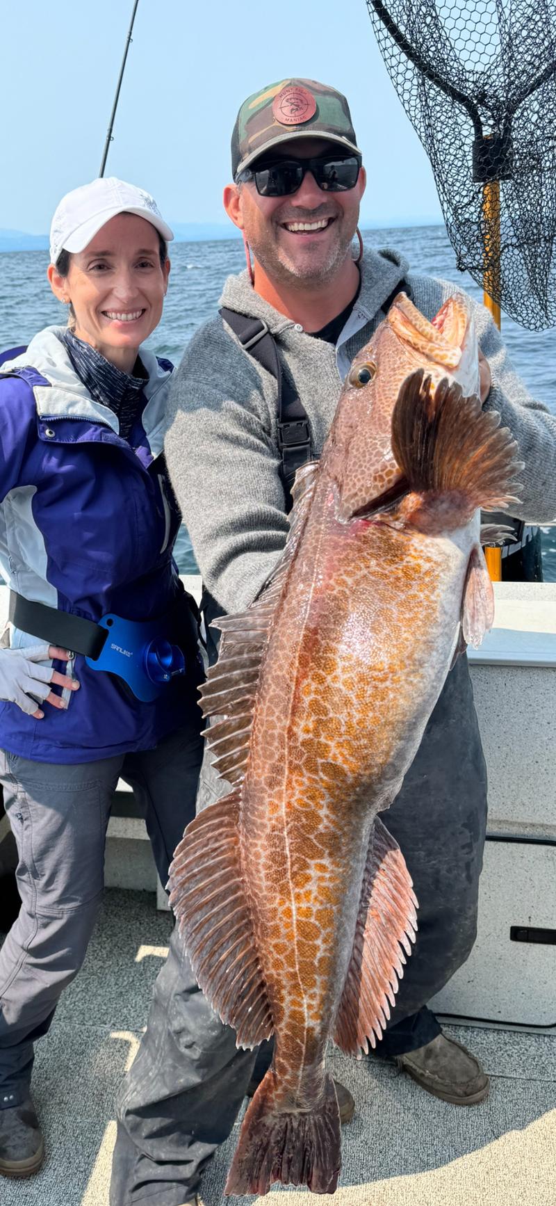 Couple holding a large lingcod on a fishing boat.