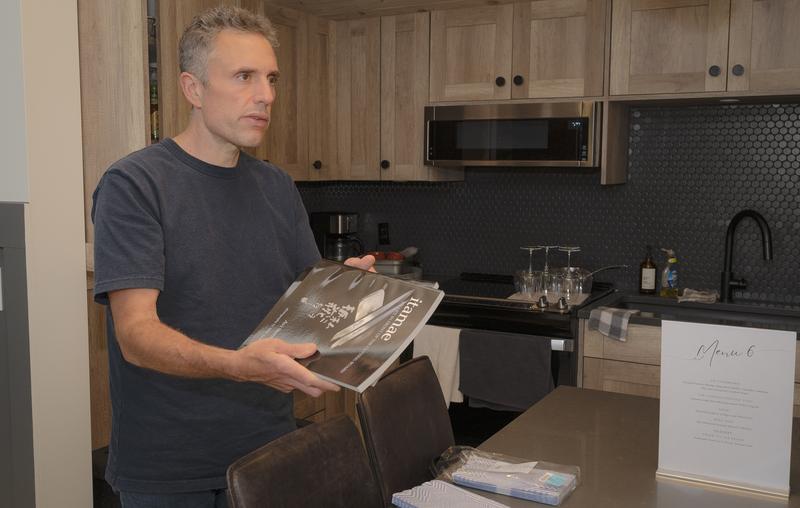 Chef holding a cook book while standing in a kitchen.