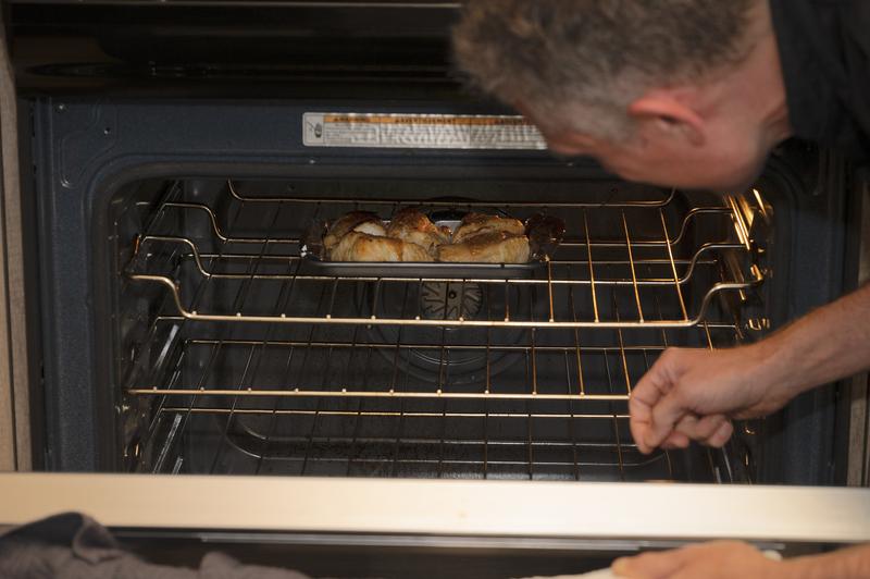 Chef looking into an open oven to check on roasting food.