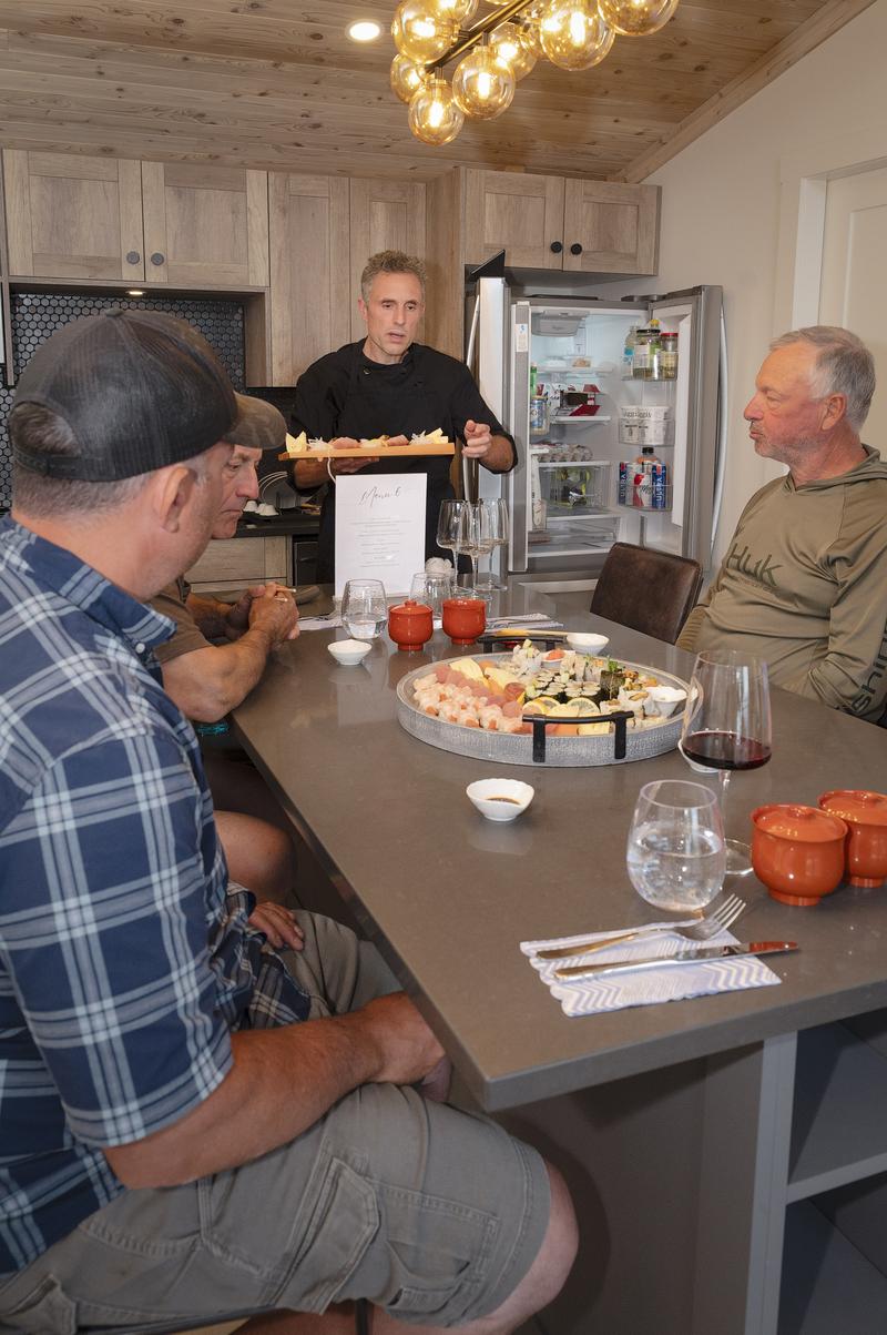 Men eating sushi at a kitchen island while a chef stands in the background.