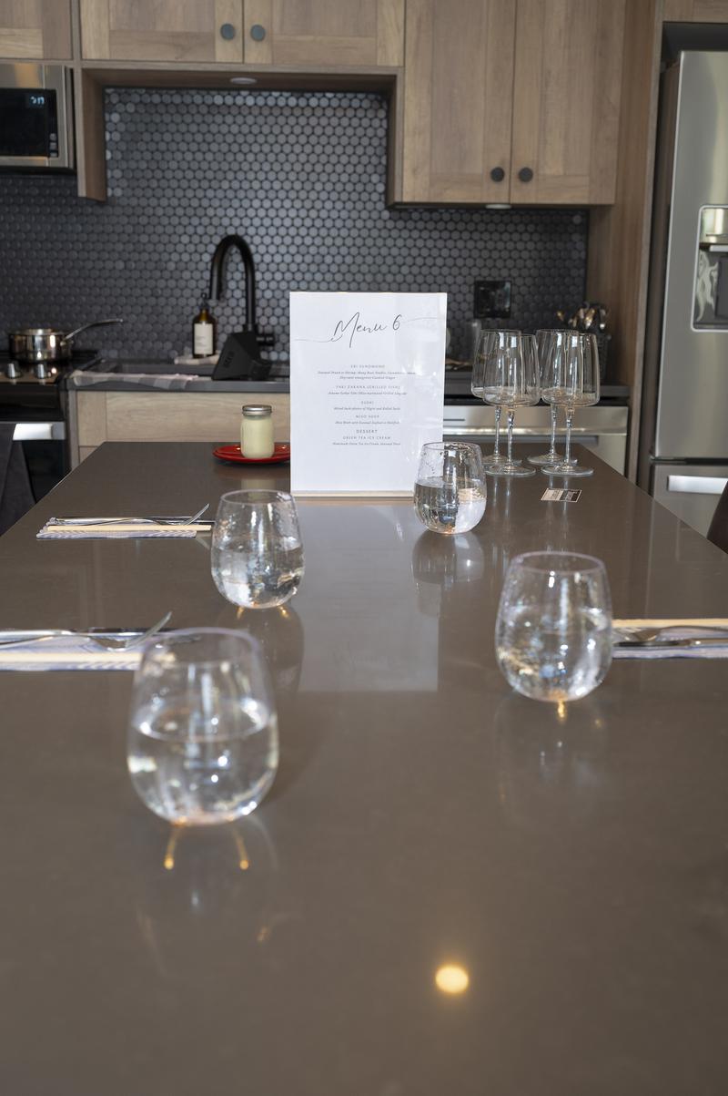 Kitchen island set for a meal with water glasses, silverware, and a standing menu card.