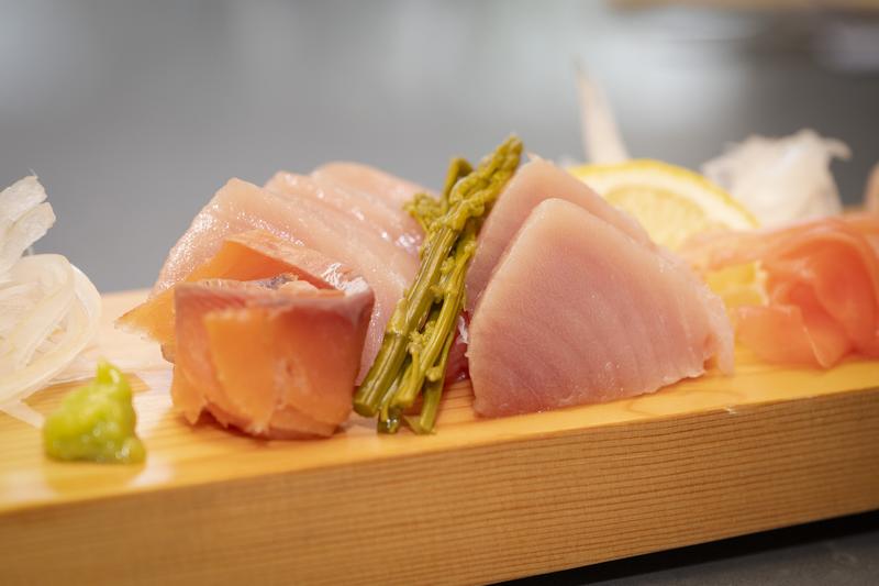 Close-up of a sashimi platter featuring salmon, tuna, asparagus, and lemon slices.