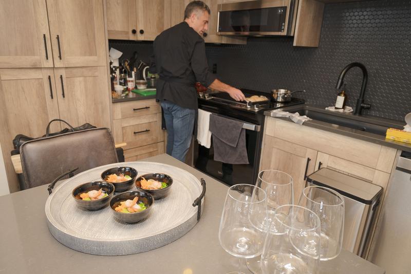 Chef cooking in a modern kitchen with appetizers and wine glasses on a nearby counter.