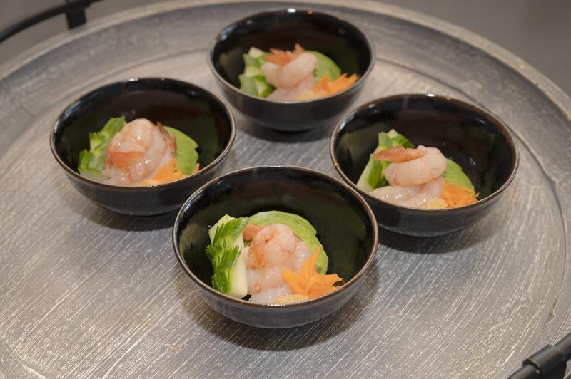 Four small black bowls containing shrimp appetizers arranged on a silver tray.