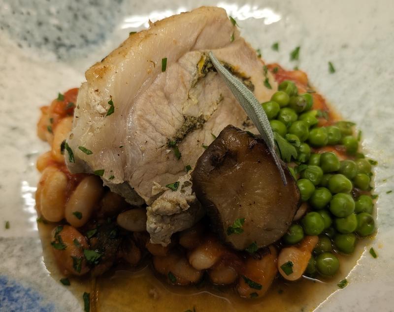 Roasted chicken breast served with potatoes, peas, and a sage leaf.