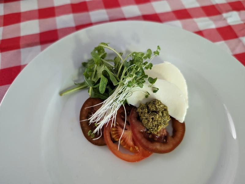 Caprese salad featuring sliced tomatoes, fresh mozzarella, arugula, and pesto.