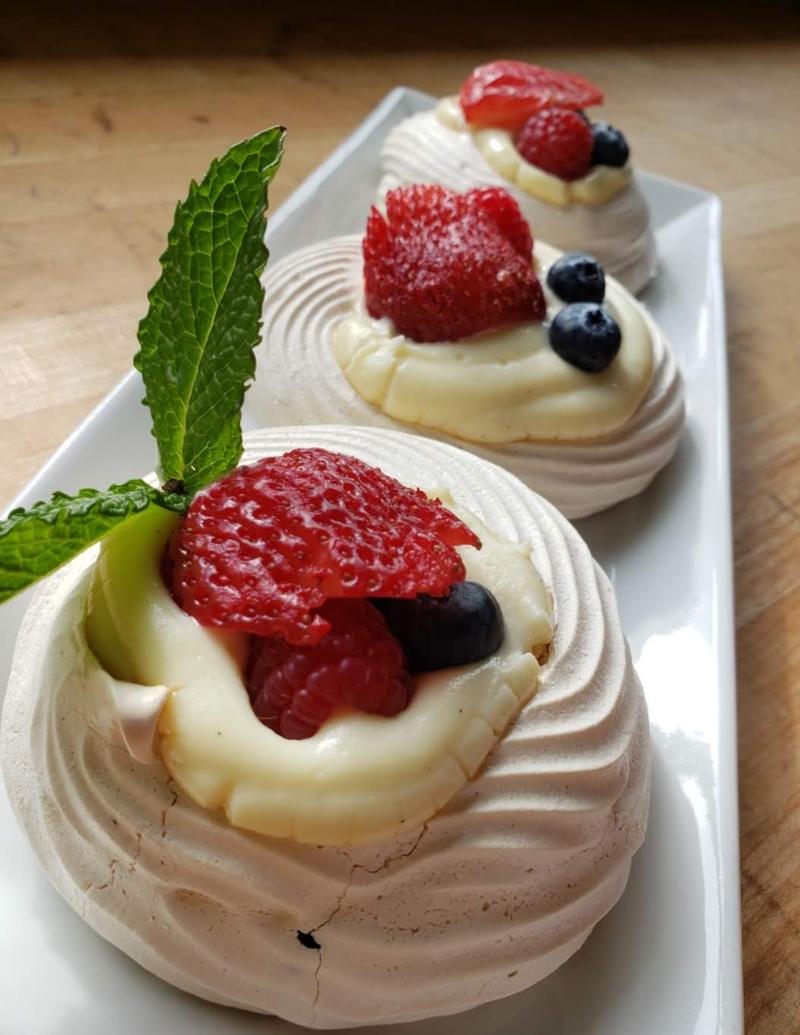 Three pavlova desserts topped with whipped cream, strawberries, blueberries, and a mint leaf.