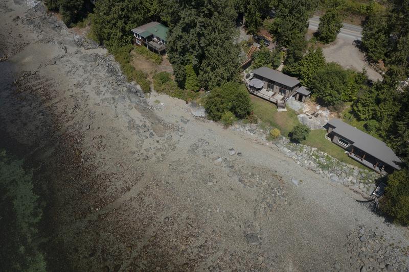 Aerial view of coastal cabins along a rocky shoreline surrounded by forest.