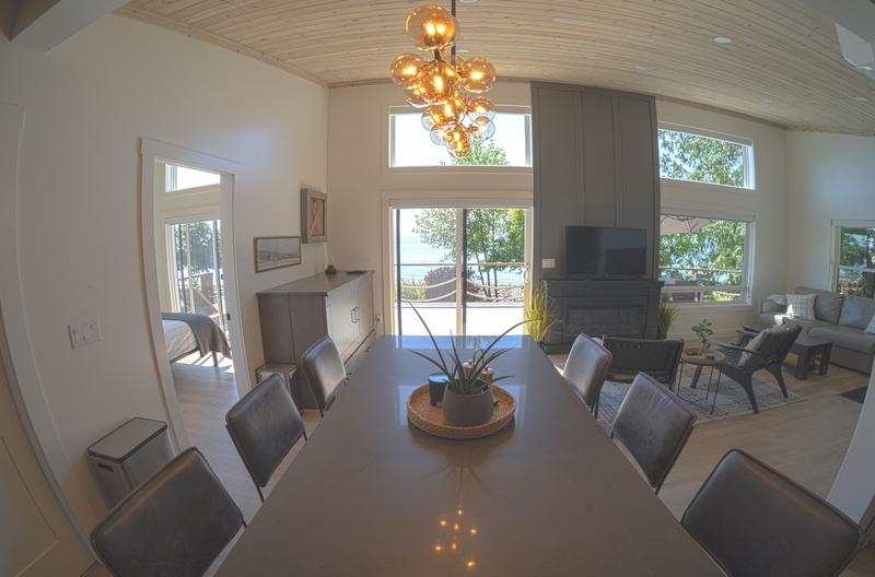 Bright dining room with a long table, modern chandelier, and large windows.